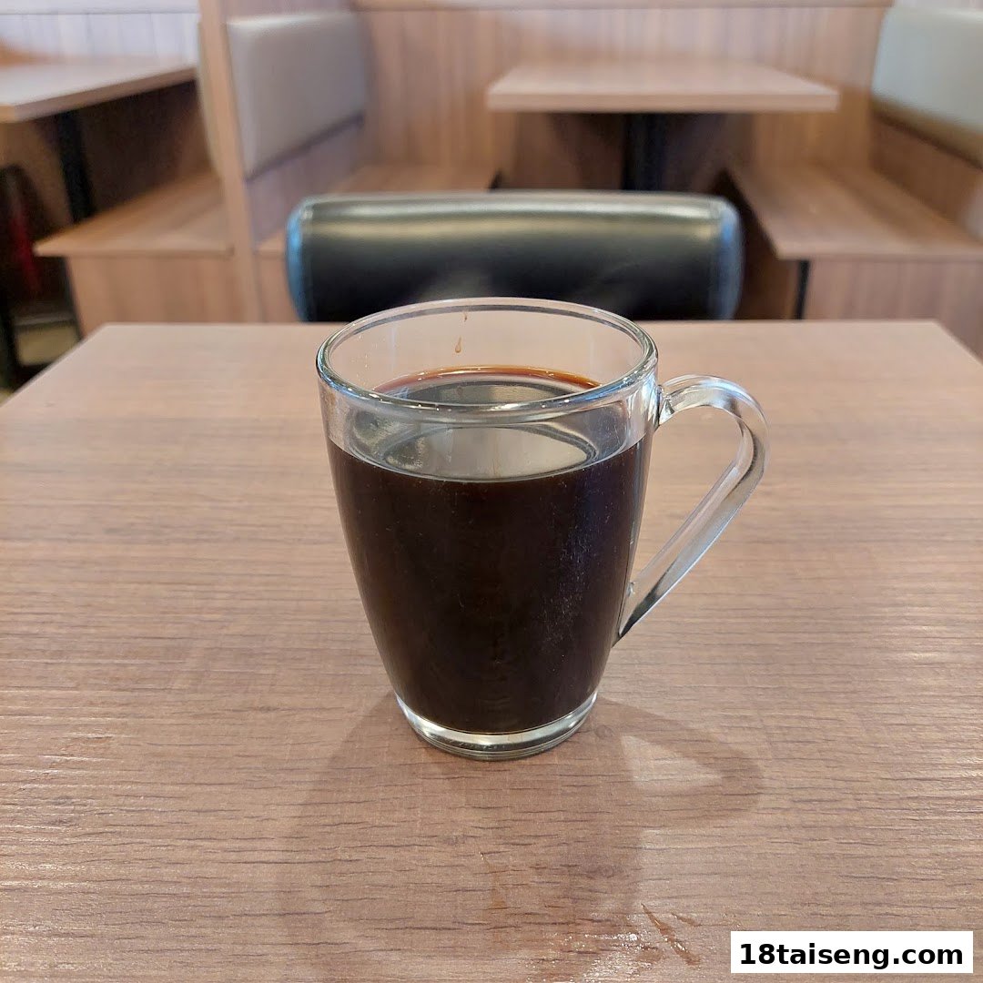 A steaming cup of coffee sits on a wooden table inside a cozy cafe with booth seating.