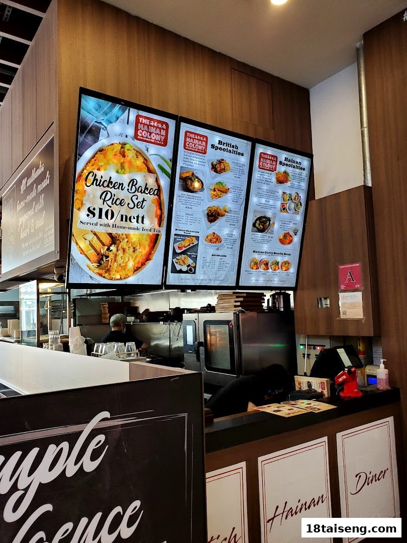 Interior view of The Hainan Colony featuring digital menu boards displaying various dishes and prices.