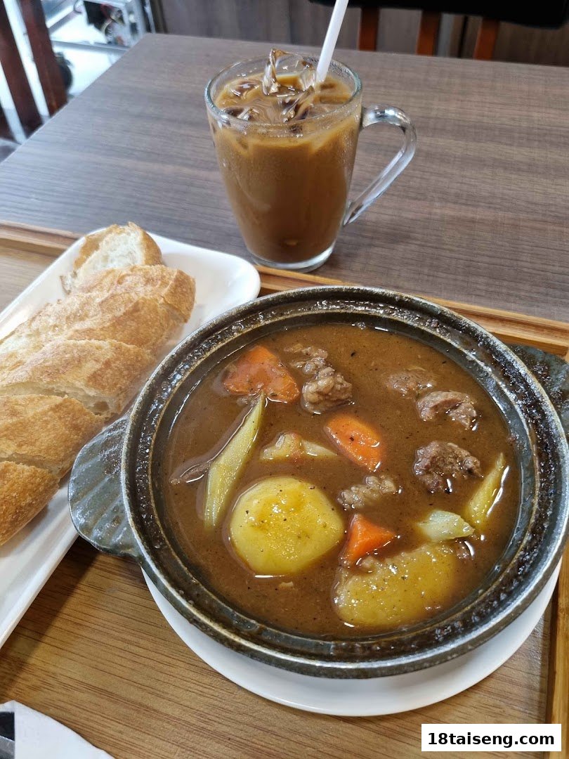 A hearty stew with potatoes, carrots, and meat, served with baguette and iced coffee.