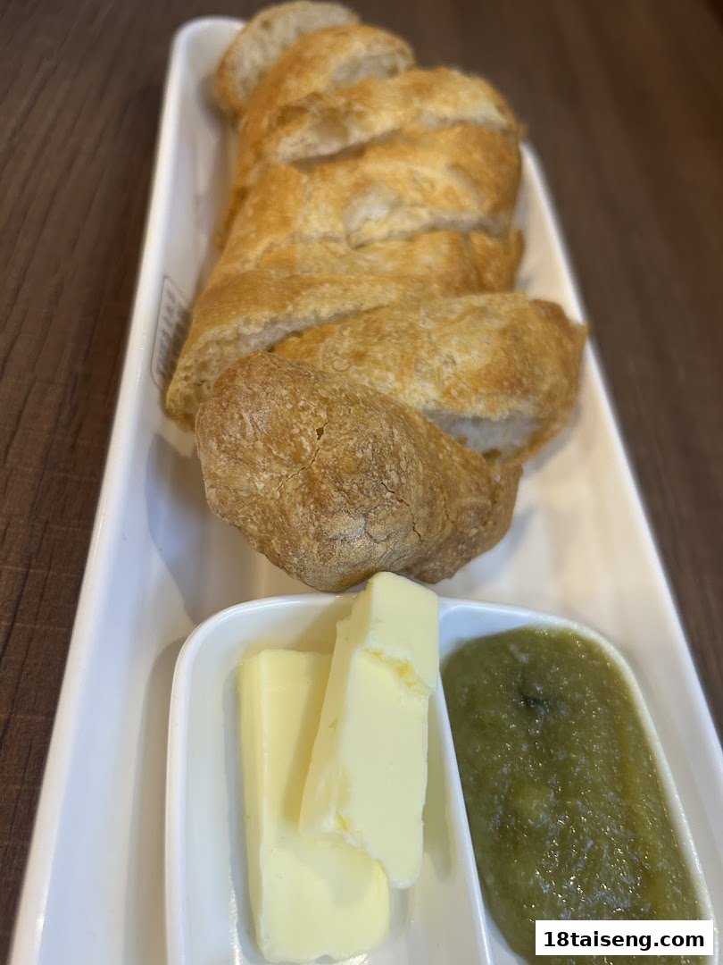 Freshly sliced bread served with butter and a green spread on a white rectangular platter.