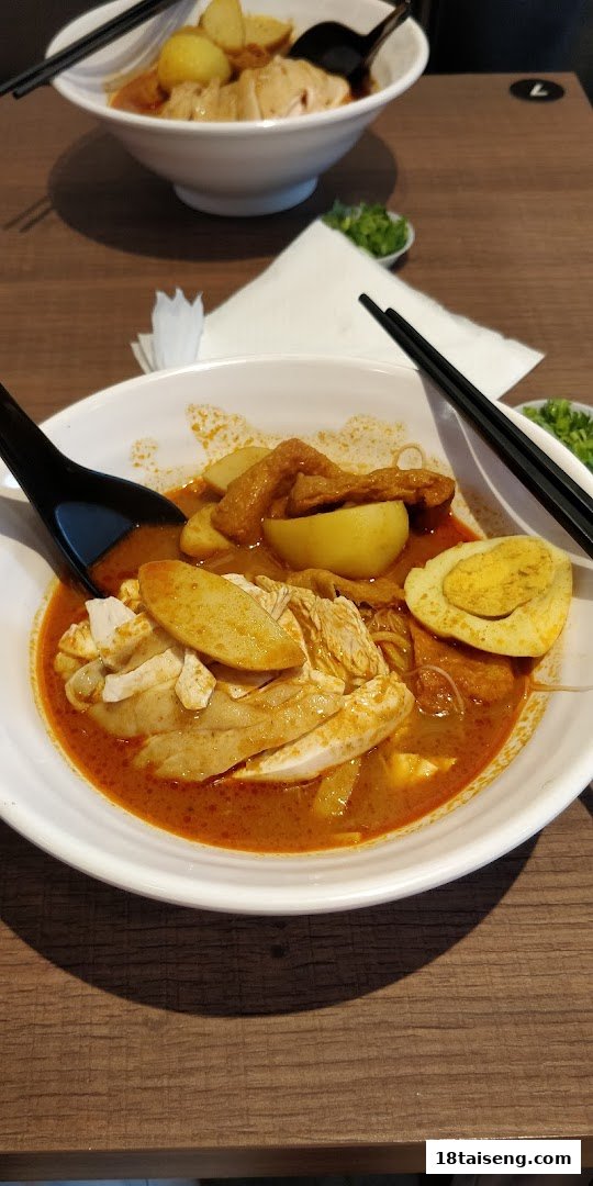 Two bowls of delicious Hainanese curry noodles with chicken, egg, and fish cakes on a wooden table.