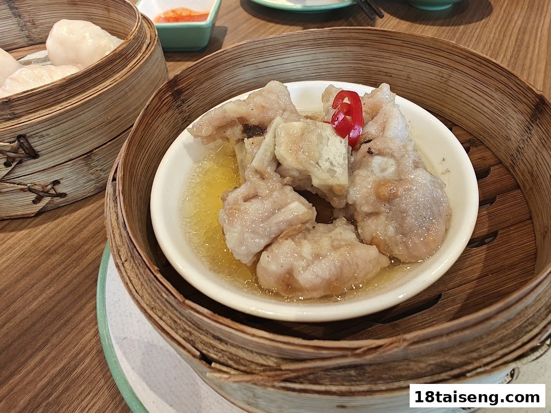 Close-up of steamed pork ribs with chili in a bamboo steamer, alongside other dim sum.