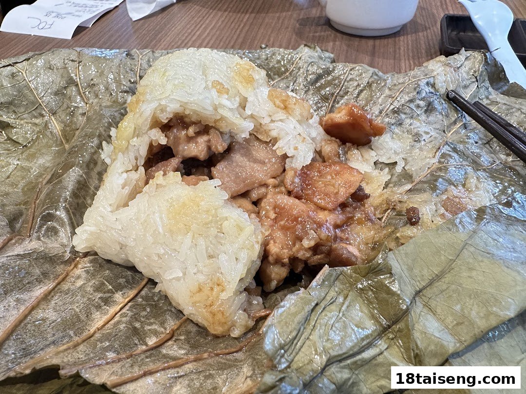 A close-up of a partially unwrapped lotus leaf-wrapped sticky rice dish with chicken, a classic dim sum.