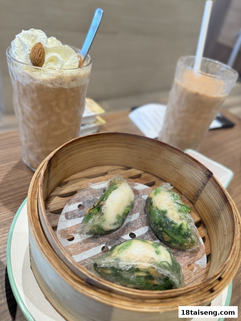 A bamboo steamer with three pieces of dim sum and two iced drinks on a table.