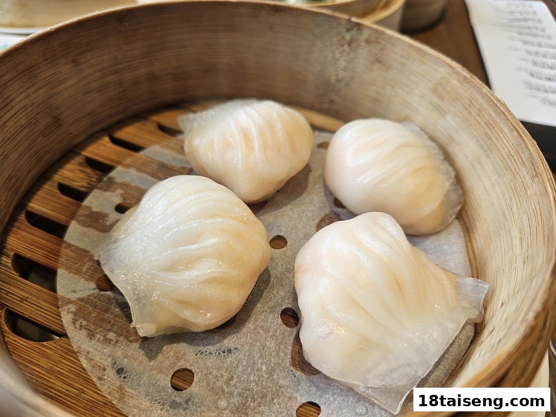 Four steamed shrimp dumplings (har gow) in a bamboo steamer, showcasing fresh dim sum.
