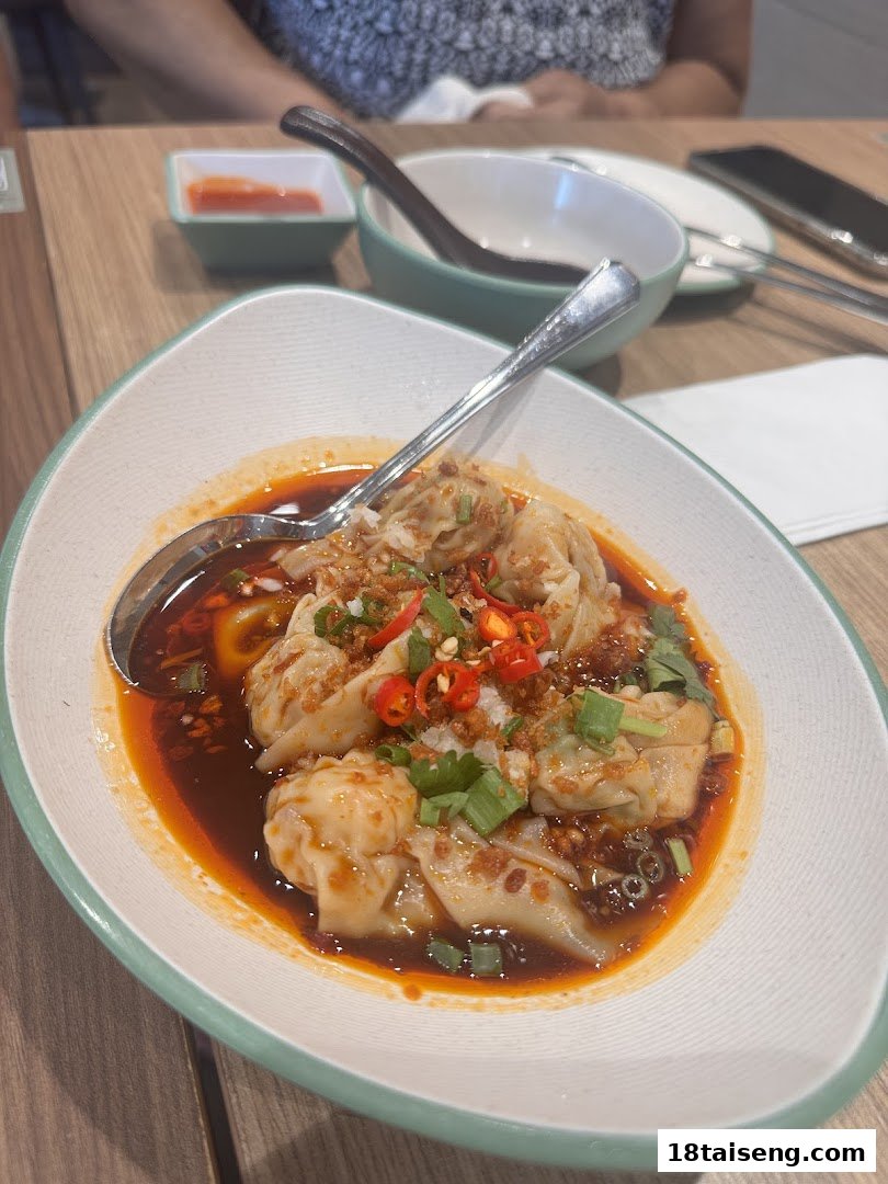 A close-up of delicious spicy wontons in chili oil, garnished with fresh herbs and chili.