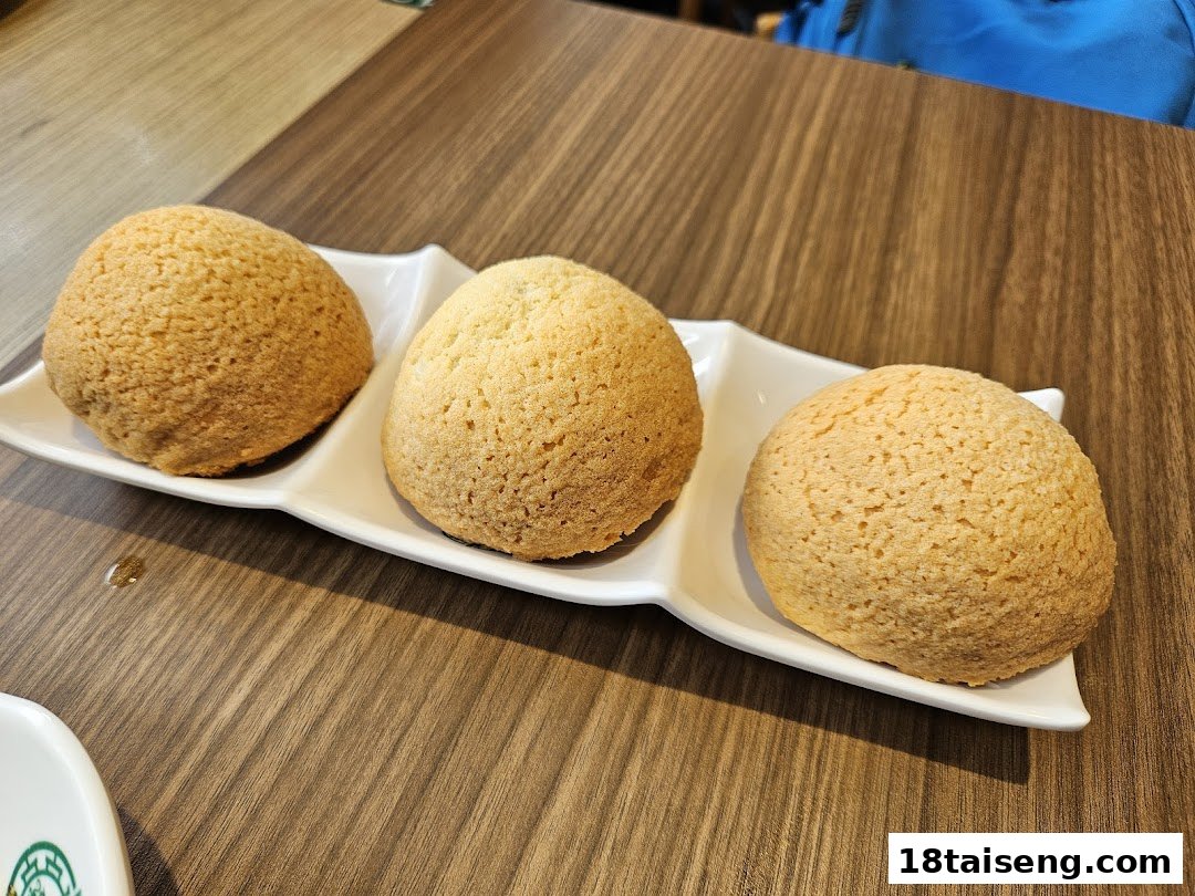 Three golden-brown baked buns with a crispy topping, served on a white plate on a wooden table.