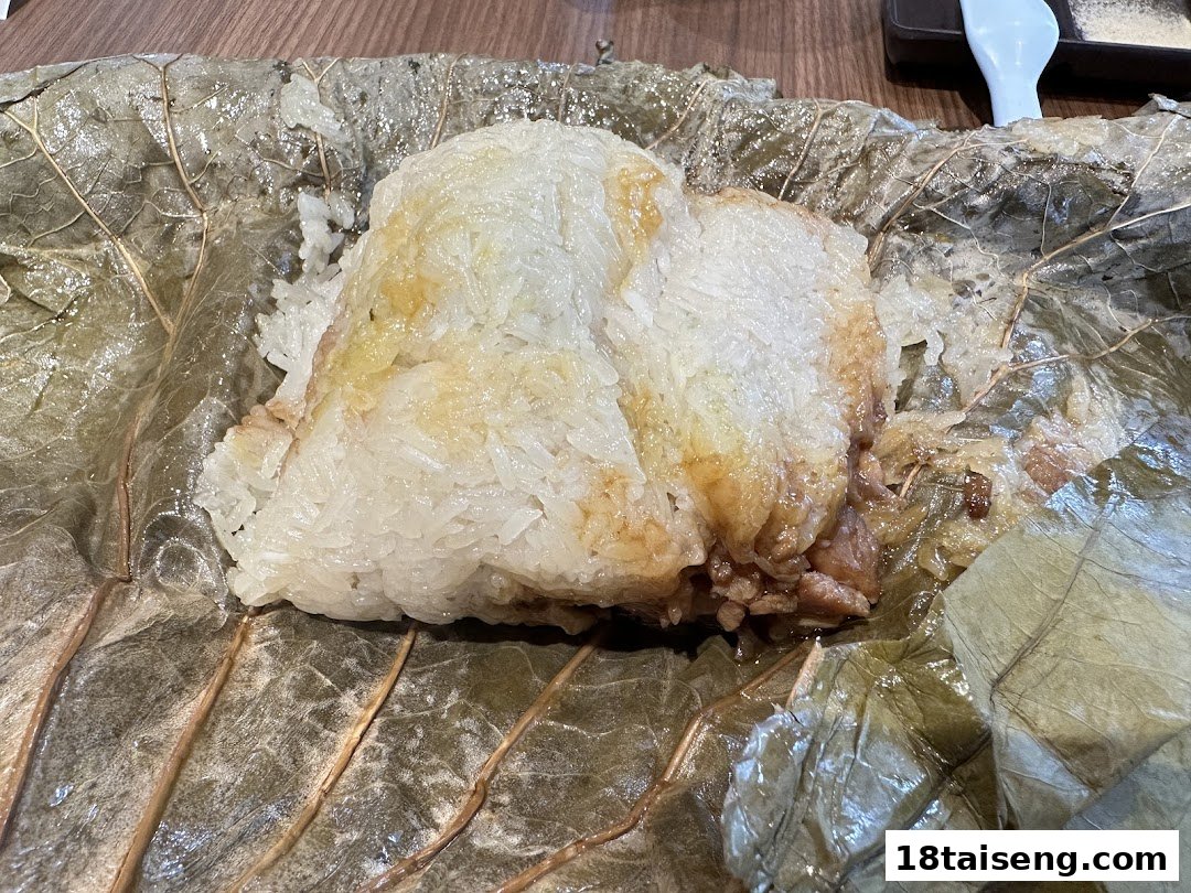 A close-up of sticky rice with filling, wrapped in a lotus leaf, served on a table.