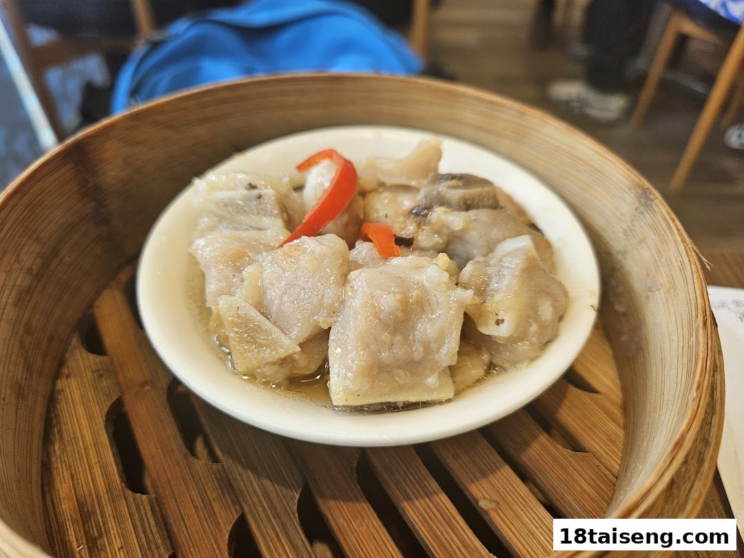A close-up of steamed pork ribs with chili in a traditional bamboo dim sum steamer.