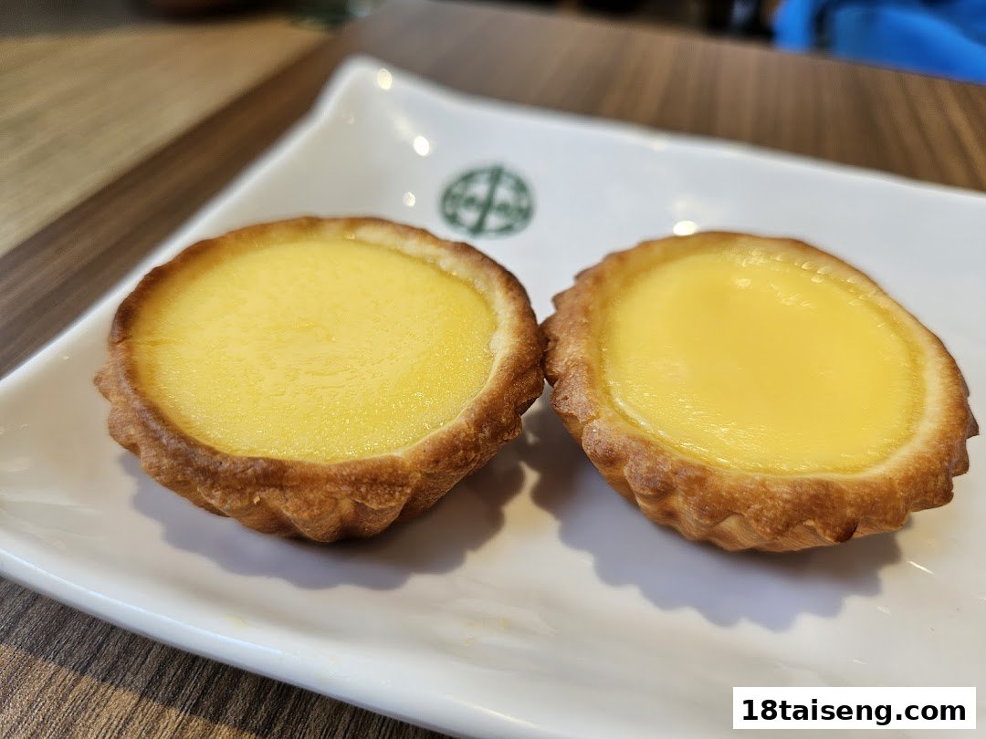 Two golden egg tarts on a white rectangular plate with the Tim Ho Wan logo.