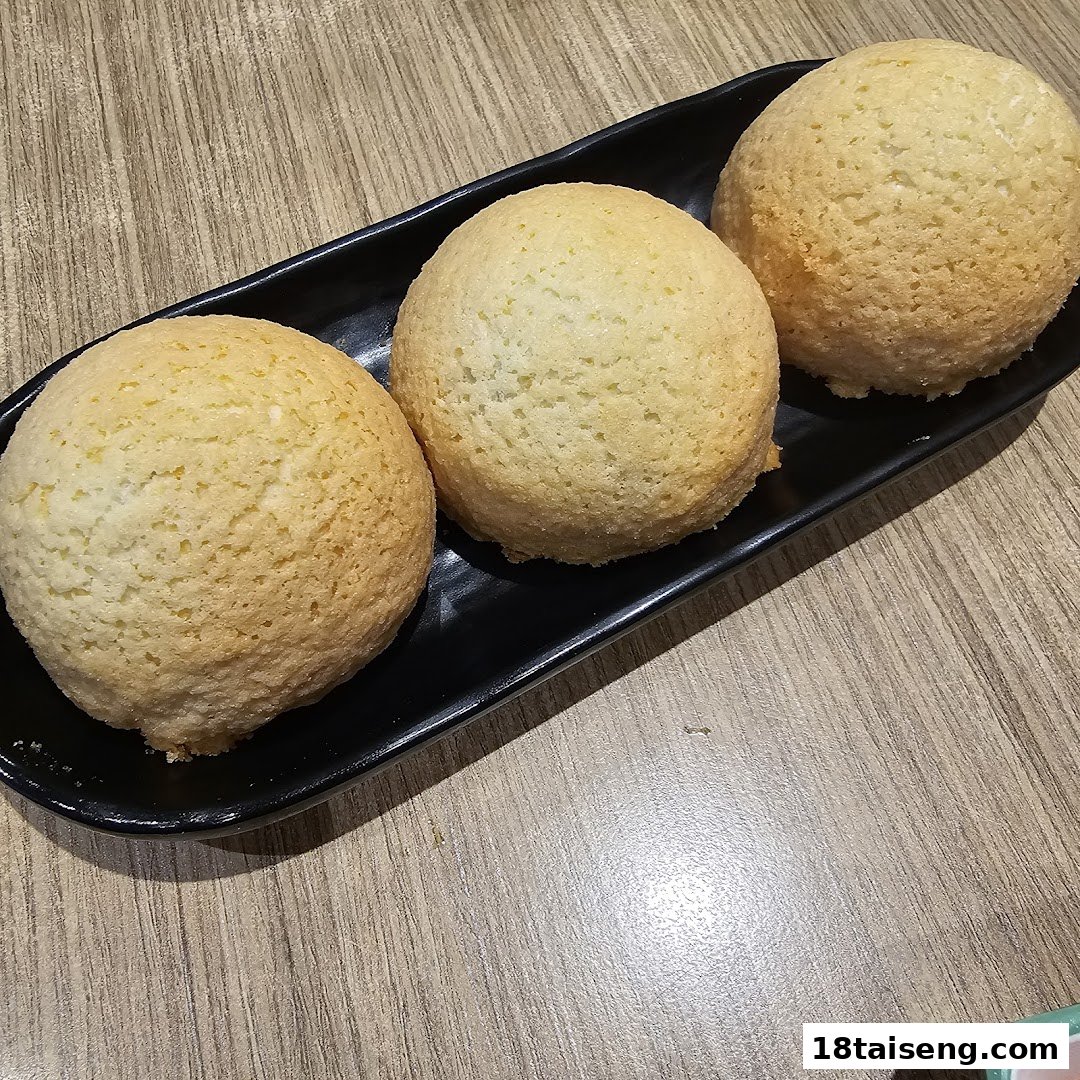 Three golden-brown baked buns served on a black rectangular plate on a wooden table.