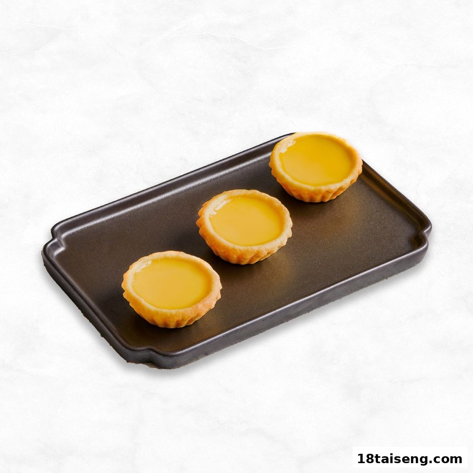 Three golden egg tarts are presented on a dark rectangular serving tray.