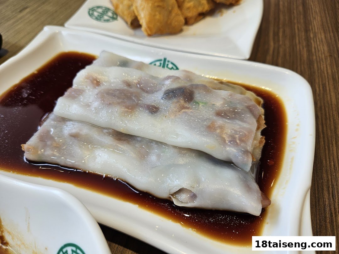 Close-up of steamed rice rolls (cheung fun) with savory sauce on a white plate.