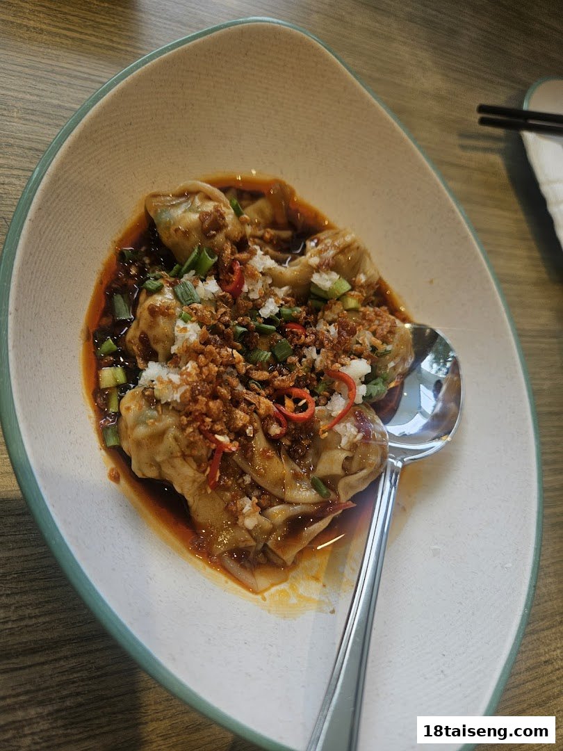 A close-up of delicious dumplings or wontons in spicy chili oil, topped with garlic and herbs.