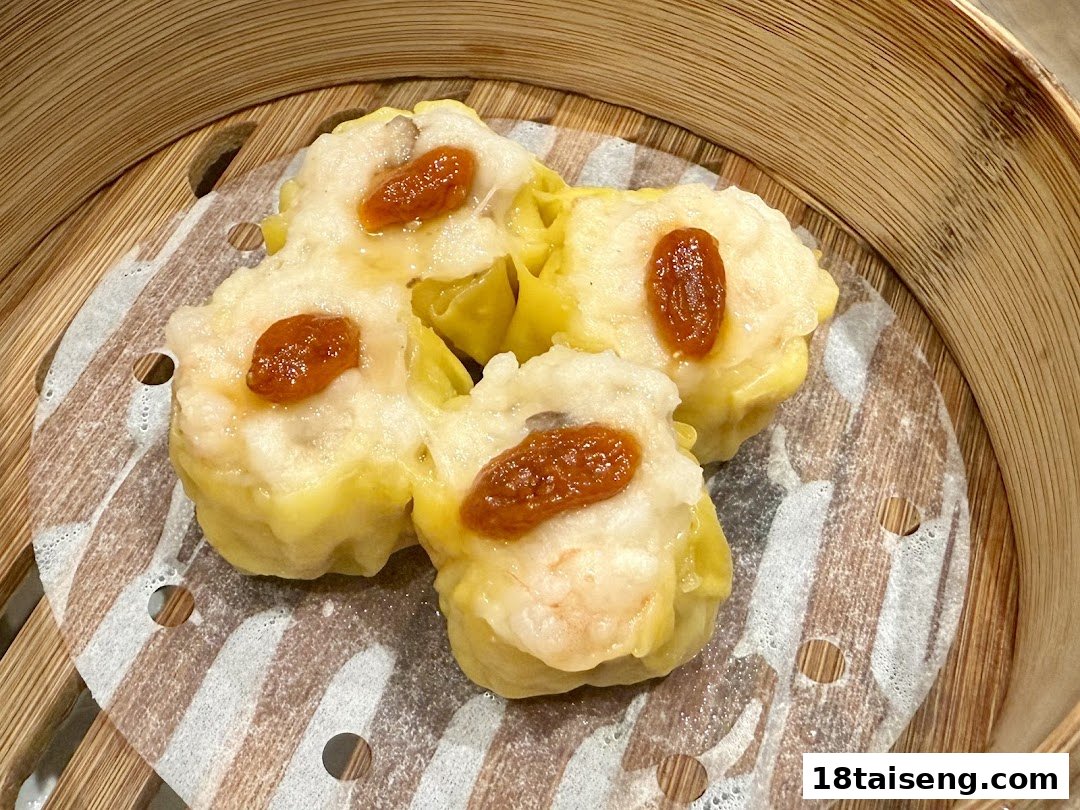 Close-up of four steamed dim sum dumplings (siu mai) with roe in a bamboo steamer.