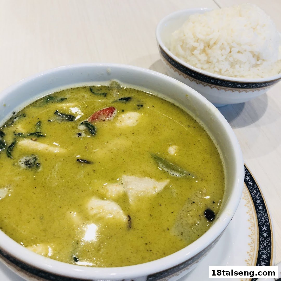 A vibrant bowl of green curry with chicken and a side of fluffy white rice.