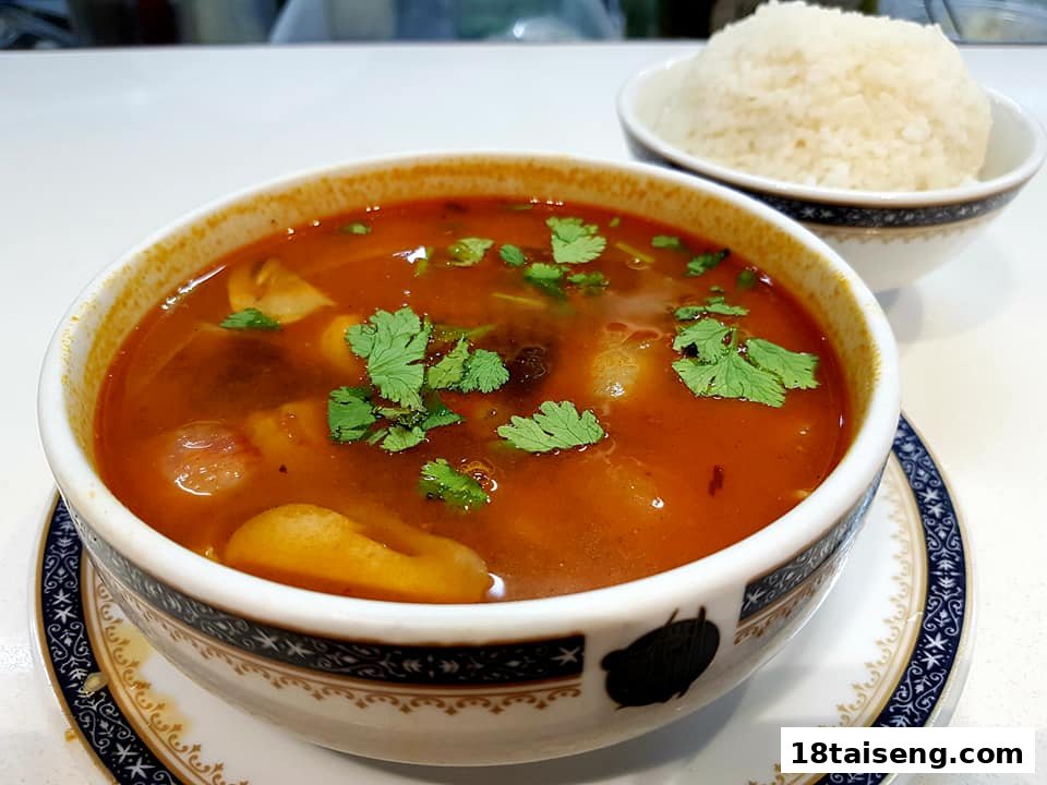 A vibrant bowl of Tom Yum soup with fresh cilantro, served with a side of rice.