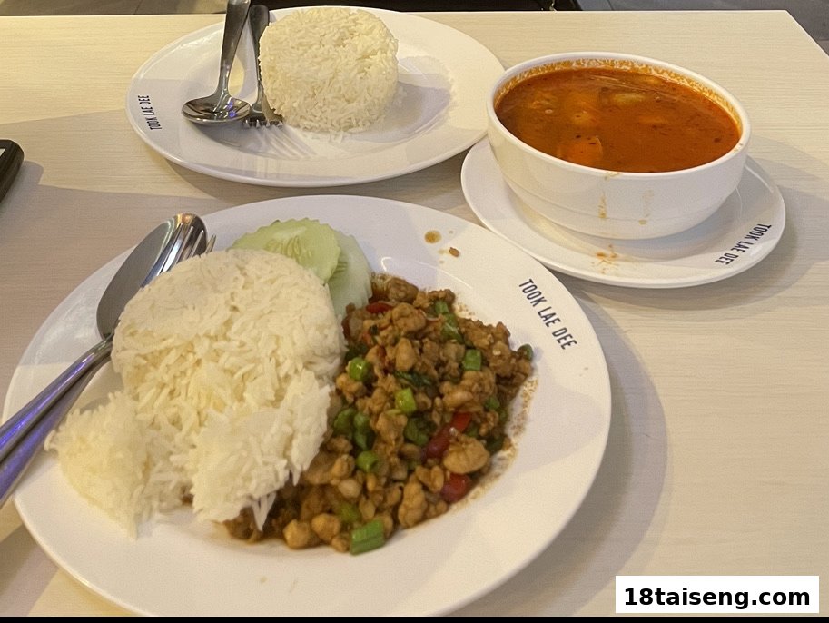A plate of stir-fried chicken with basil and rice, alongside a bowl of tom yum soup.