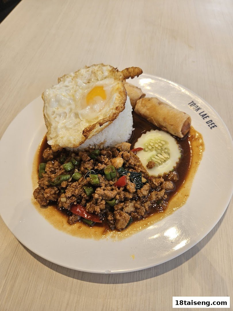 A plate of Thai basil pork with rice, a fried egg, and spring rolls from Took Lae Dee.