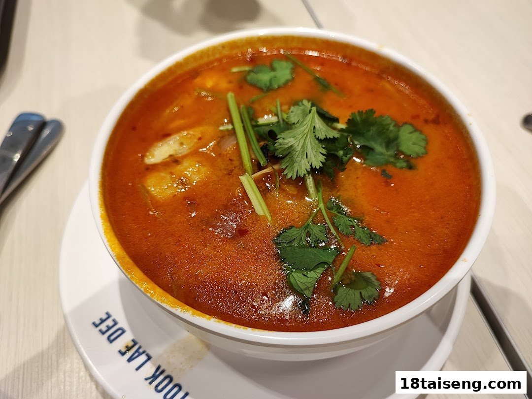 A vibrant bowl of spicy Thai soup, likely Tom Yum, garnished with fresh herbs.