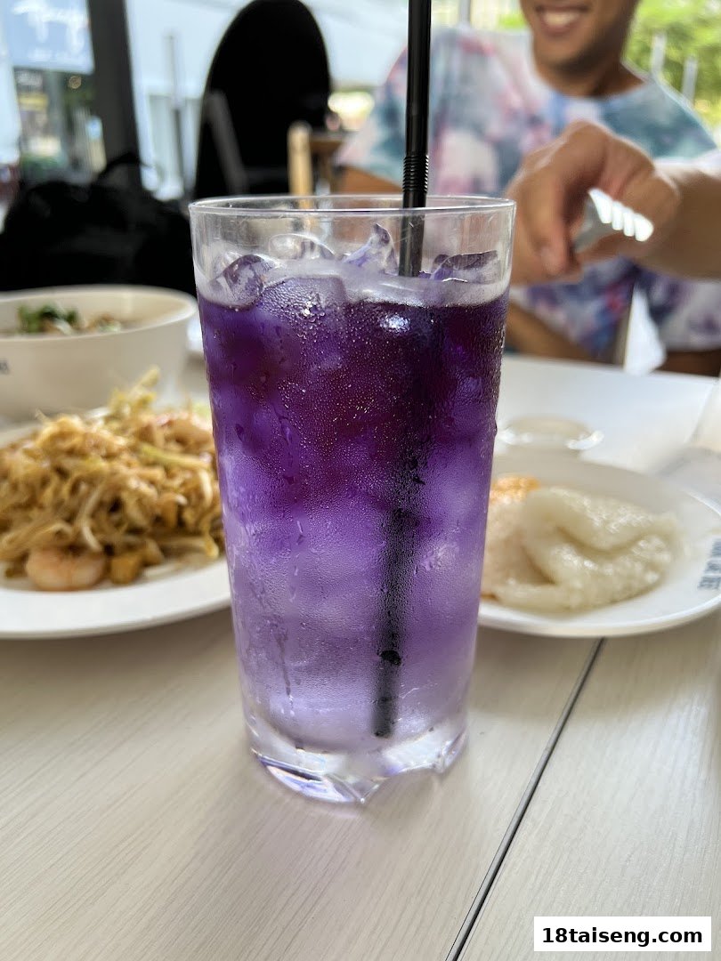A vibrant purple drink with ice, noodles, and a dessert on a table at Took Lae Dee.