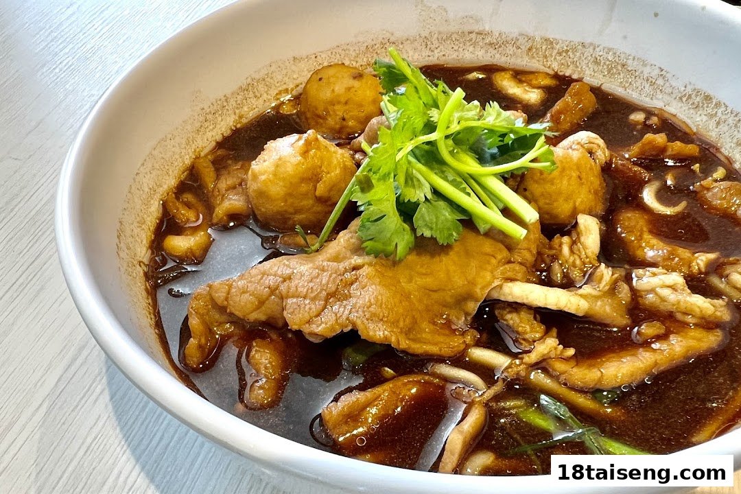 A close-up of a rich, dark broth noodle dish with meat, meatballs, and fresh cilantro.