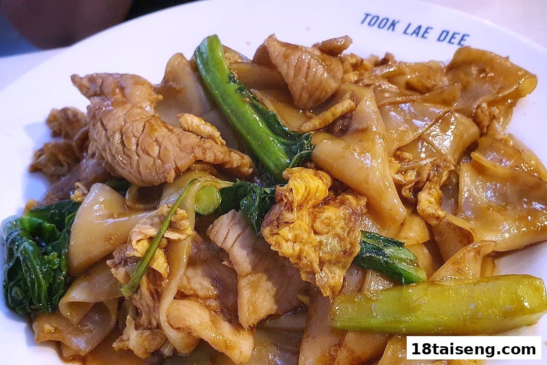 A close-up of a delicious stir-fried noodle dish with pork, egg, and green vegetables.