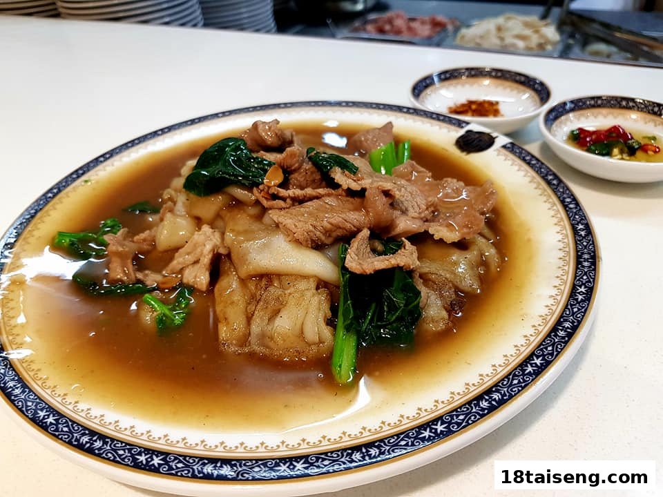 A close-up of a delicious plate of stir-fried noodles with beef and greens in savory gravy.