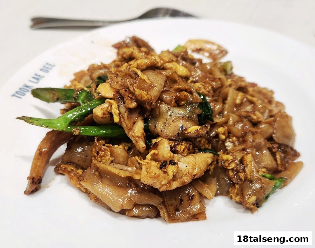 A close-up of a delicious plate of stir-fried noodles with chicken and greens from Took Lae Dee.
