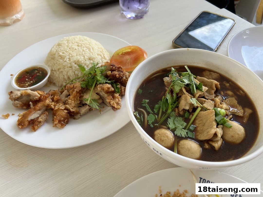 A plate of fried chicken with rice and a bowl of noodle soup on a table.