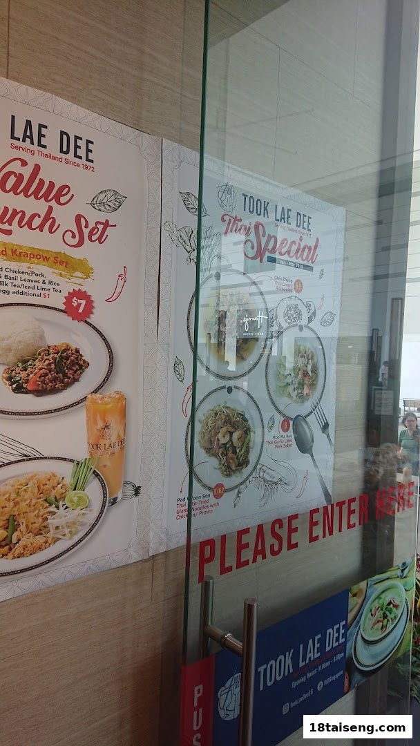 Promotional posters for Took Lae Dee's Thai specials and lunch sets displayed on the shop's glass entrance.