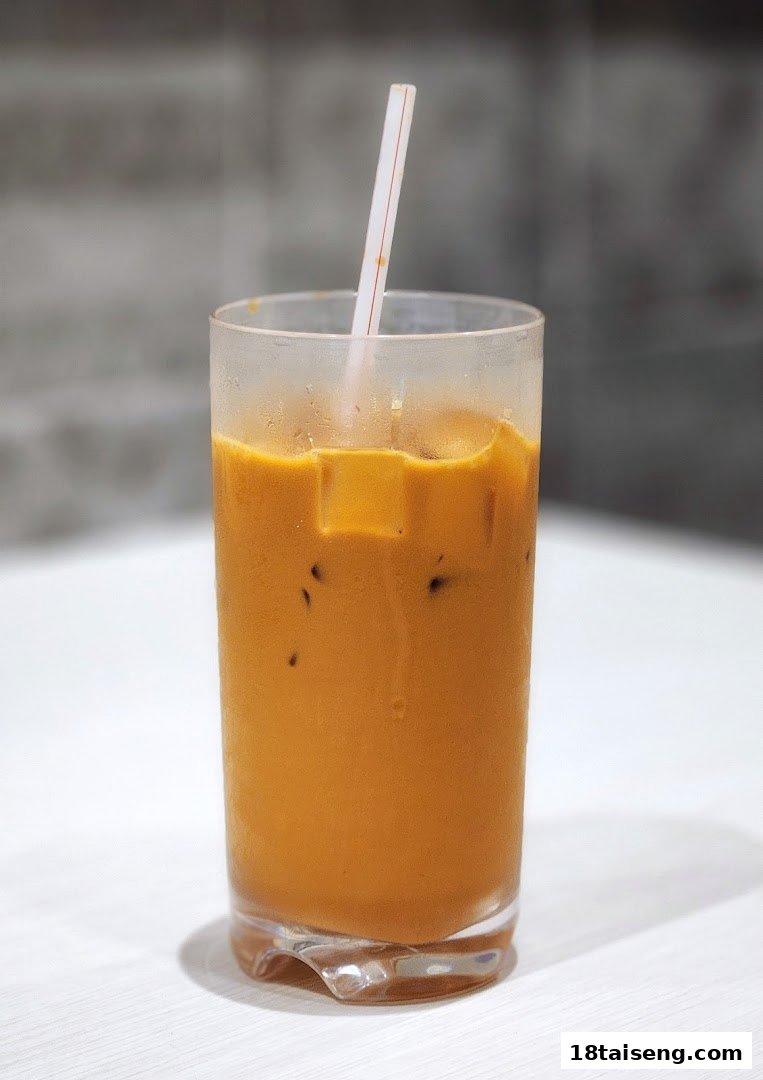 A refreshing glass of iced Thai milk tea with a straw on a white table.