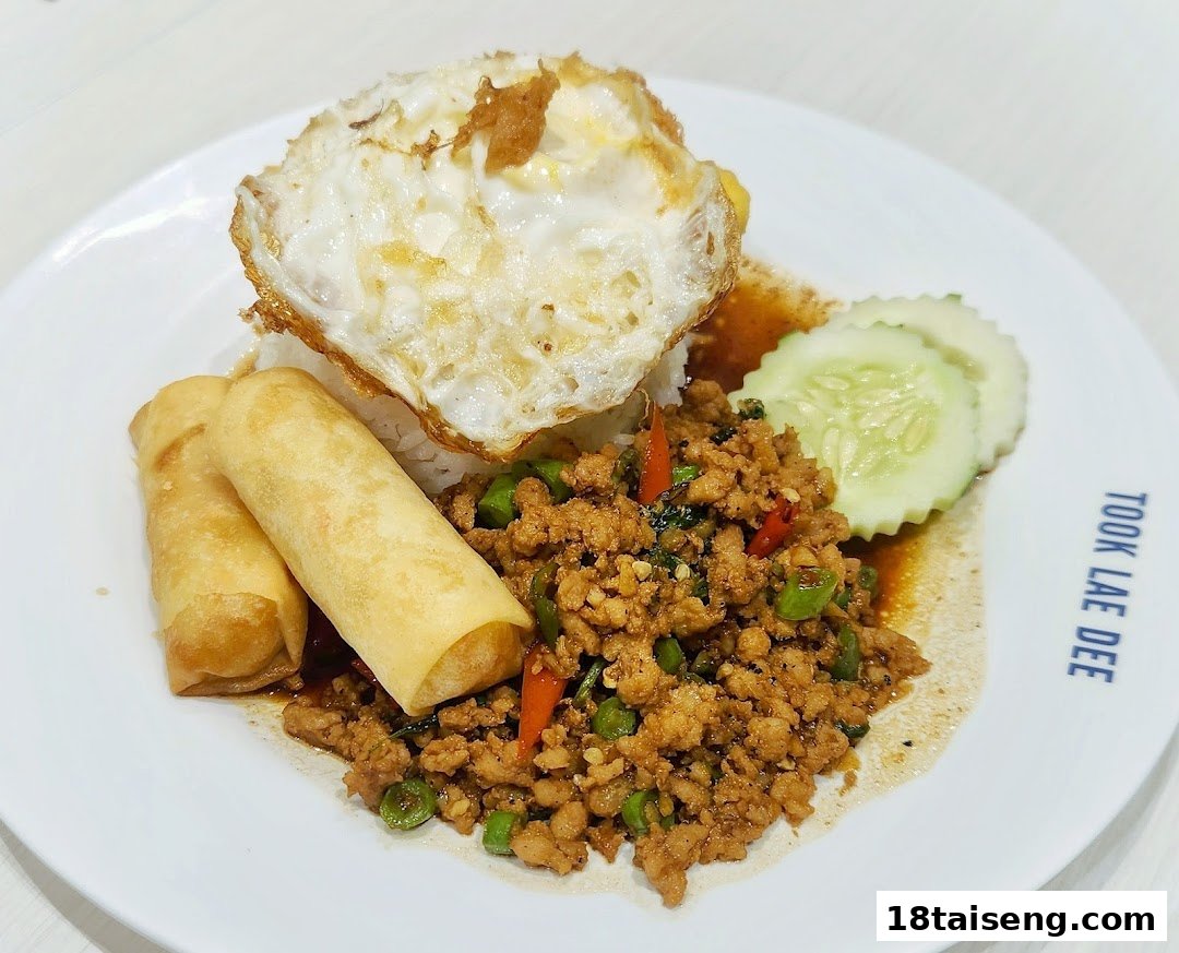 A delicious plate of Thai basil minced pork with rice, fried egg, and spring rolls.