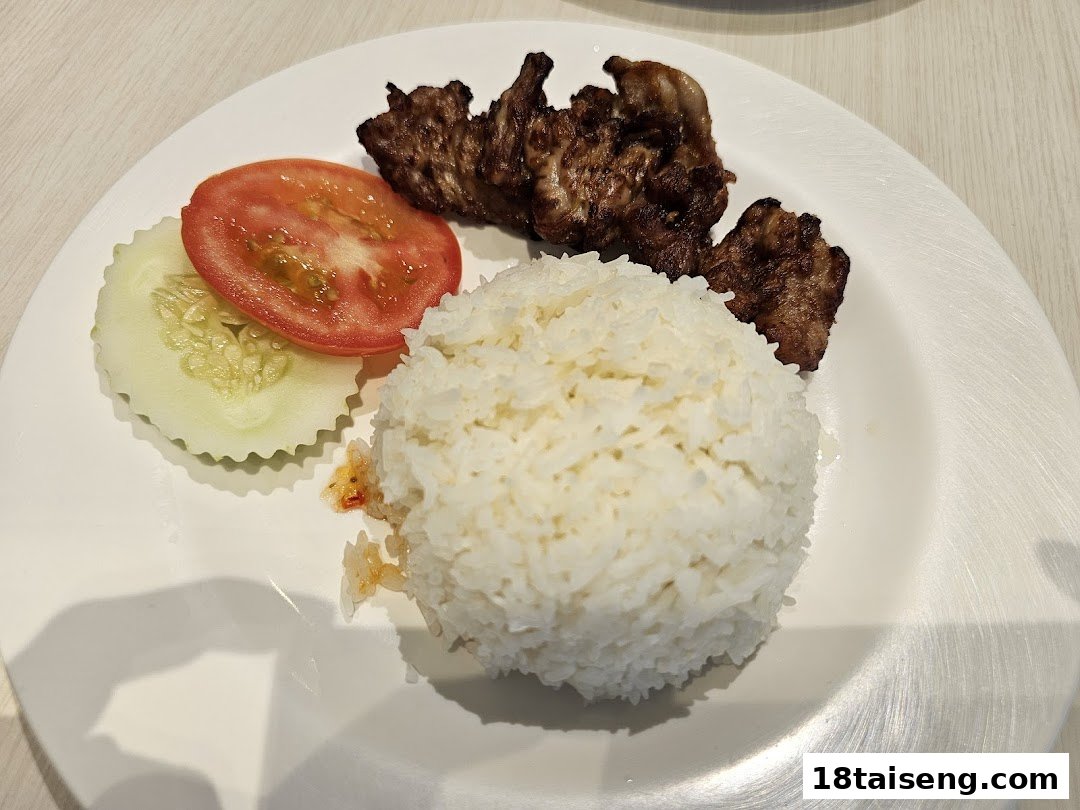 A plate of grilled meat with a mound of white rice, fresh tomato, and cucumber slices.