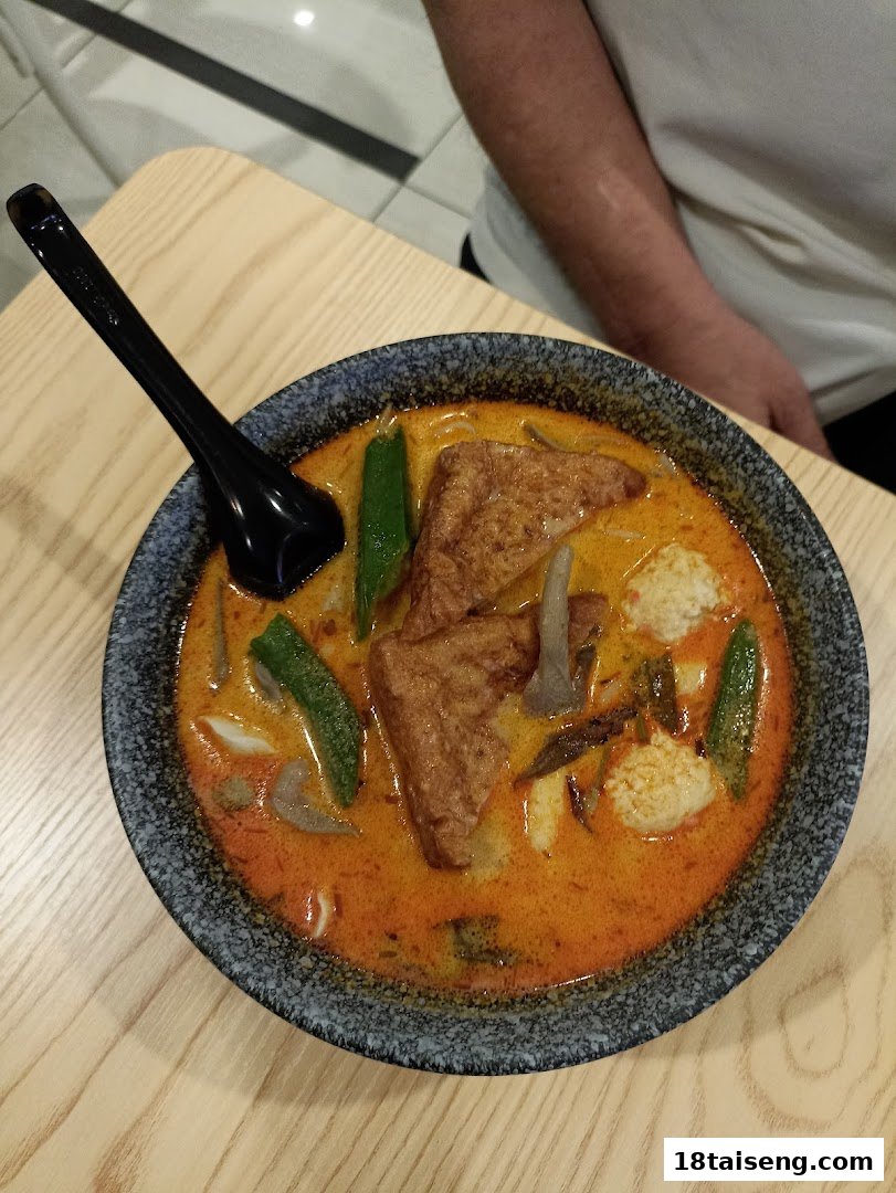 A vibrant bowl of vegetarian curry or laksa with tofu, okra, and other fresh ingredients on a wooden table.