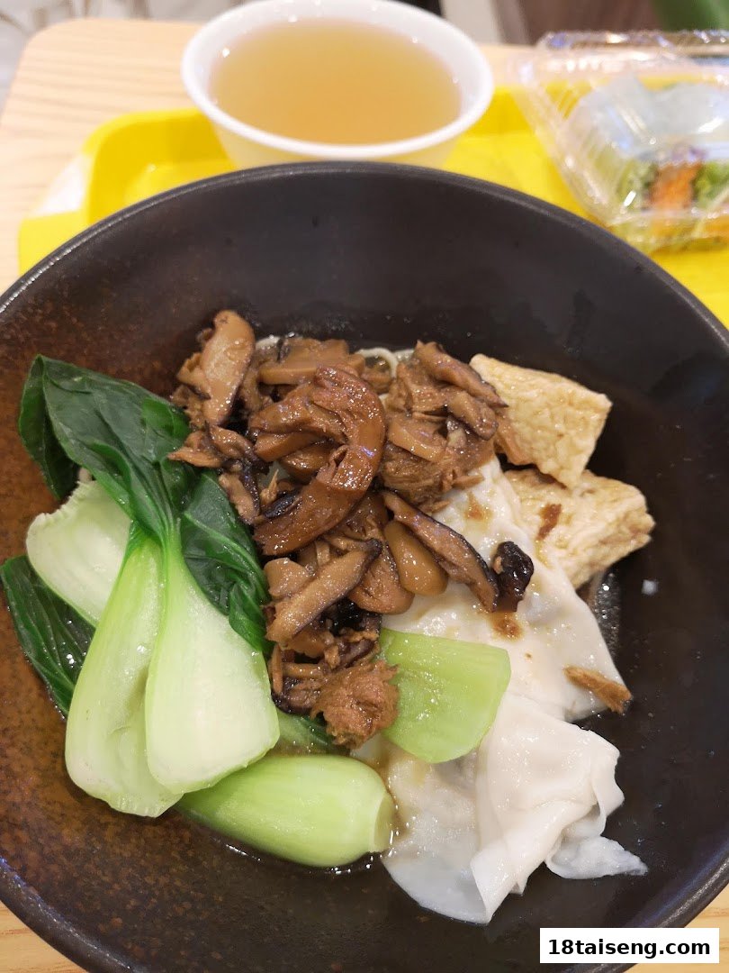 A close-up of a delicious vegetarian noodle dish with mushrooms, bok choy, and dumplings, served with soup.
