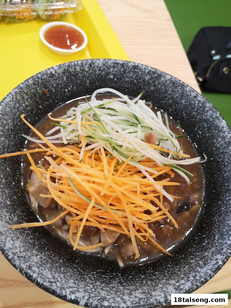 A close-up of a delicious vegetarian dish with shredded carrots and cucumbers in a dark bowl.