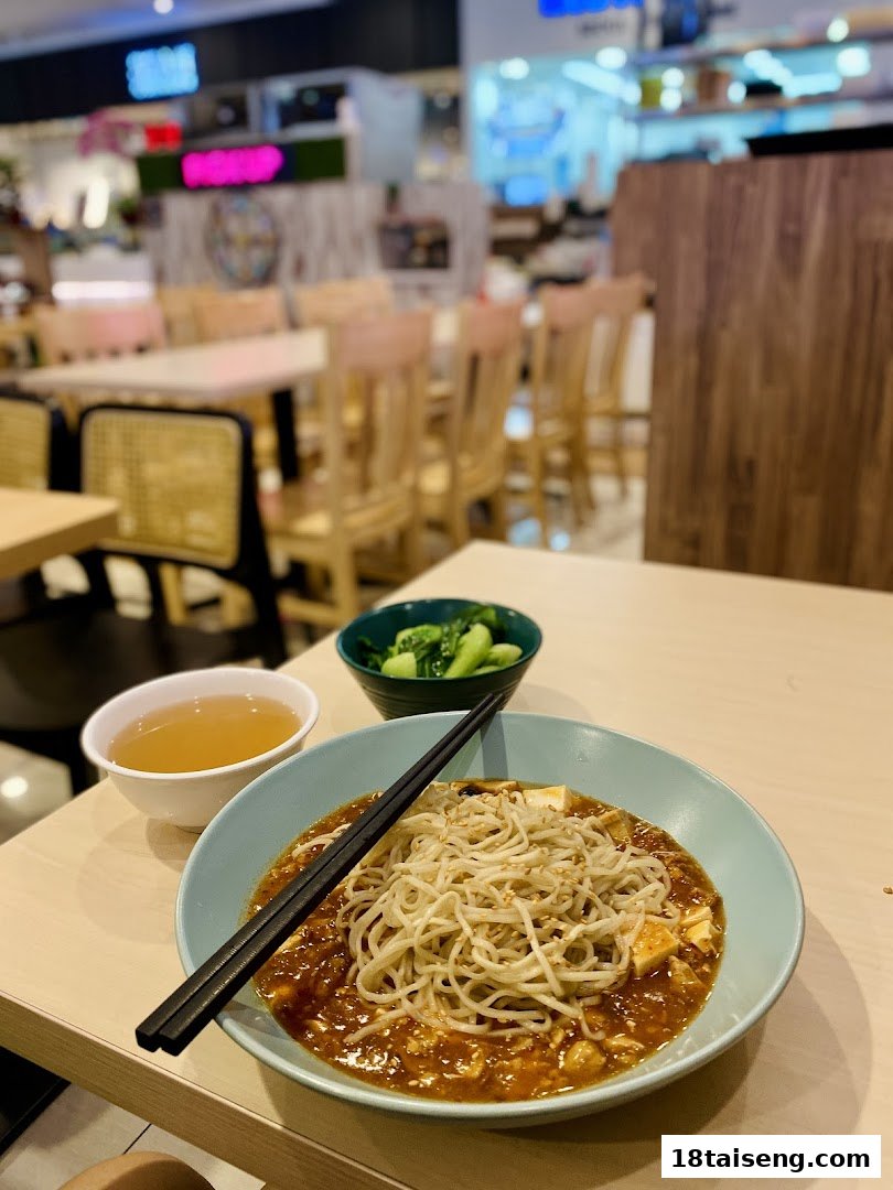 A delicious bowl of vegetarian noodles with a side of vegetables and soup on a table.