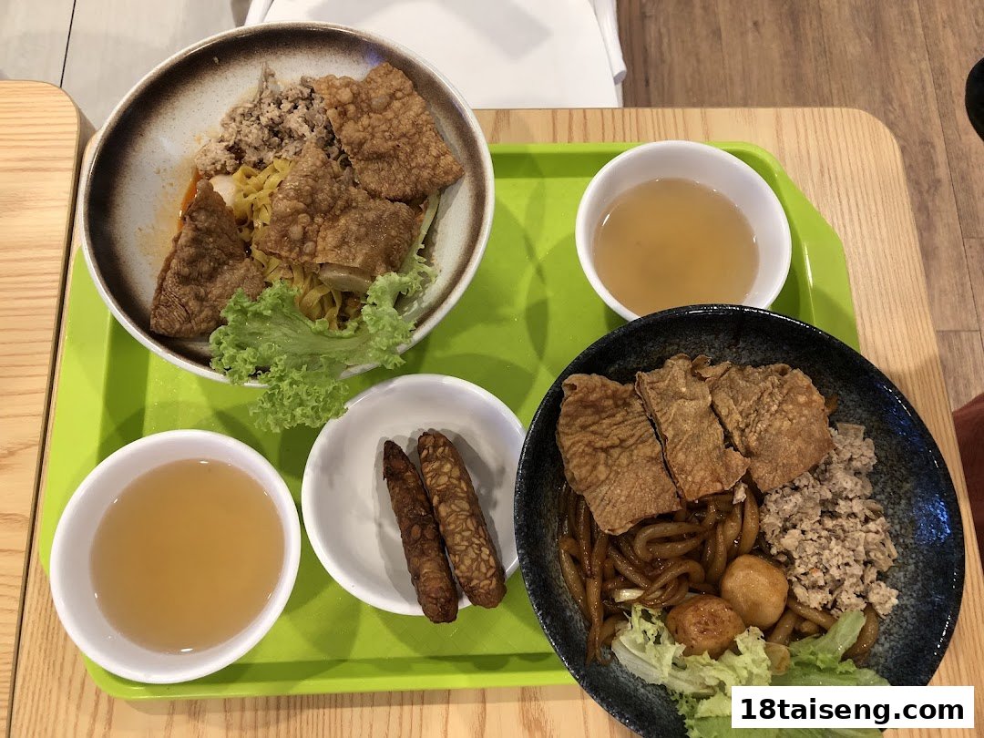 Two vibrant bowls of vegetarian noodles with mock meat, served with soup and sides on a green tray.