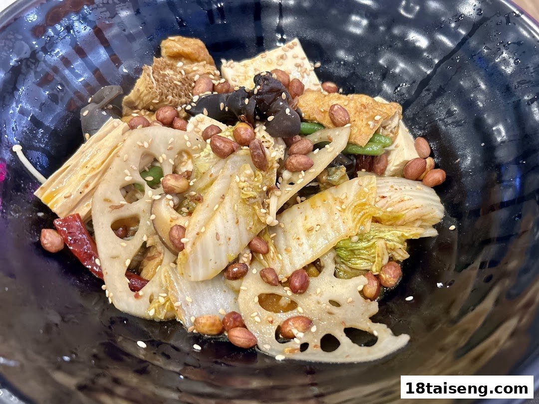A close-up of a vibrant vegetarian dish featuring lotus root, peanuts, and various vegetables in a black bowl.