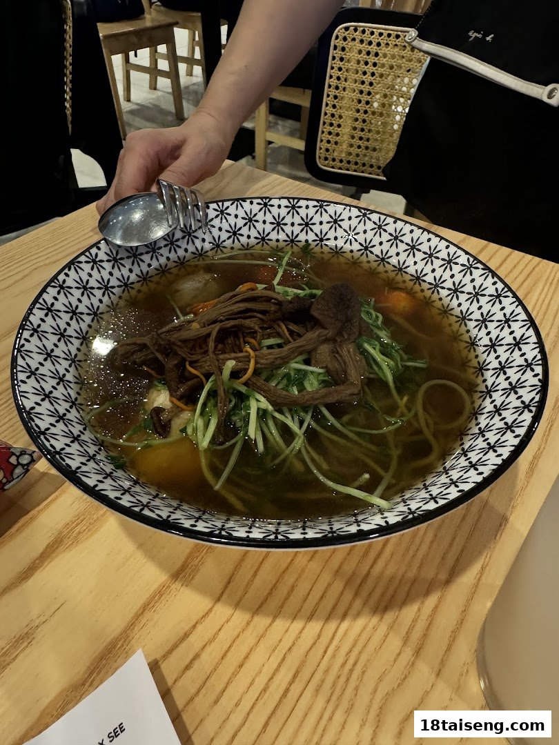 A close-up of a vibrant bowl of vegetarian noodles with mushrooms and fresh greens on a wooden table.