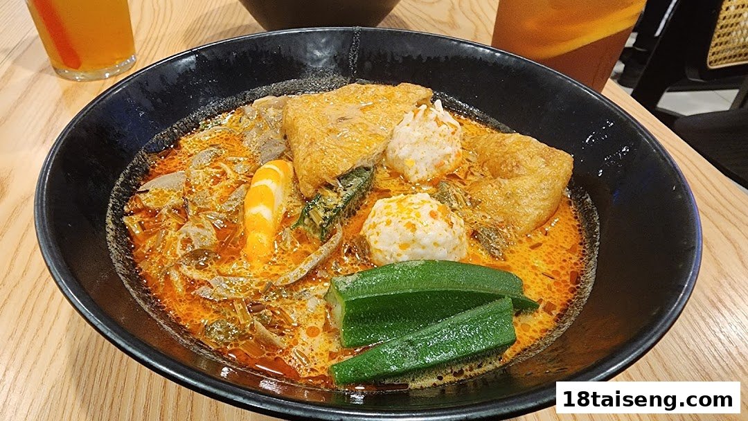 A vibrant bowl of vegetarian curry or laksa with tofu, mock meat, and okra on a wooden table.