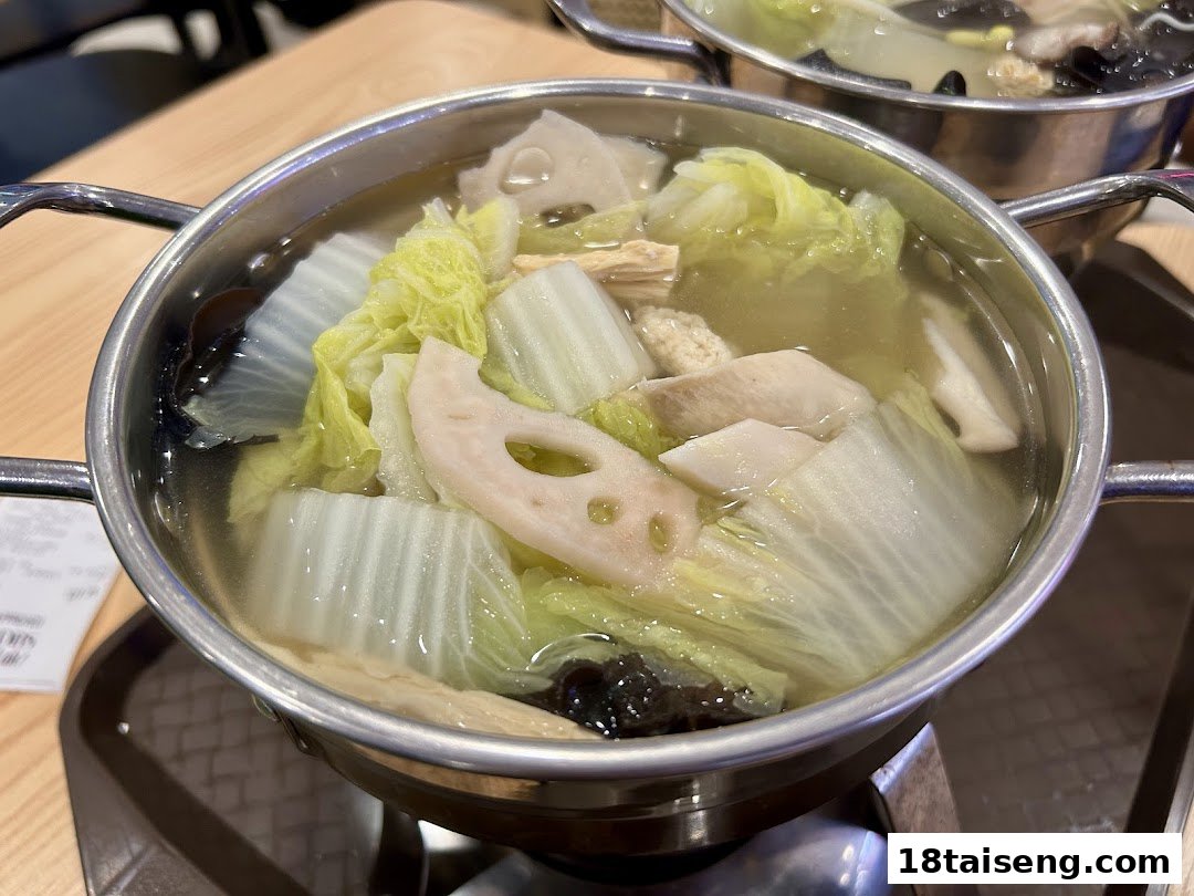A close-up of a hot pot filled with various vegetables like cabbage, lotus root, and mushrooms.