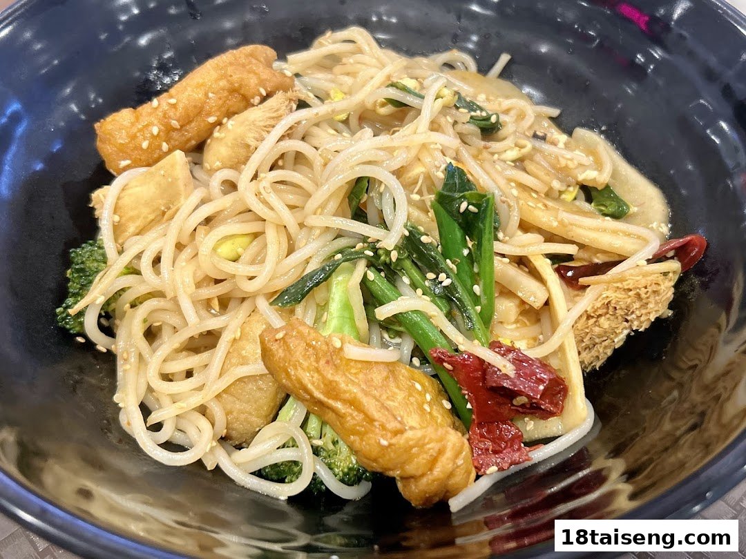 A close-up of a vibrant vegetarian noodle dish with various vegetables and mock meat.