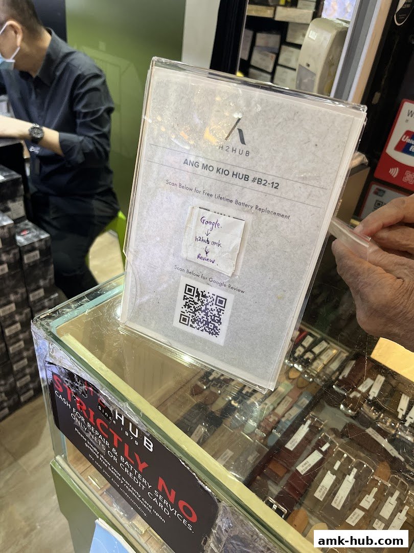 A sign offering free lifetime battery replacement with a QR code for Google reviews at H2 HUB.