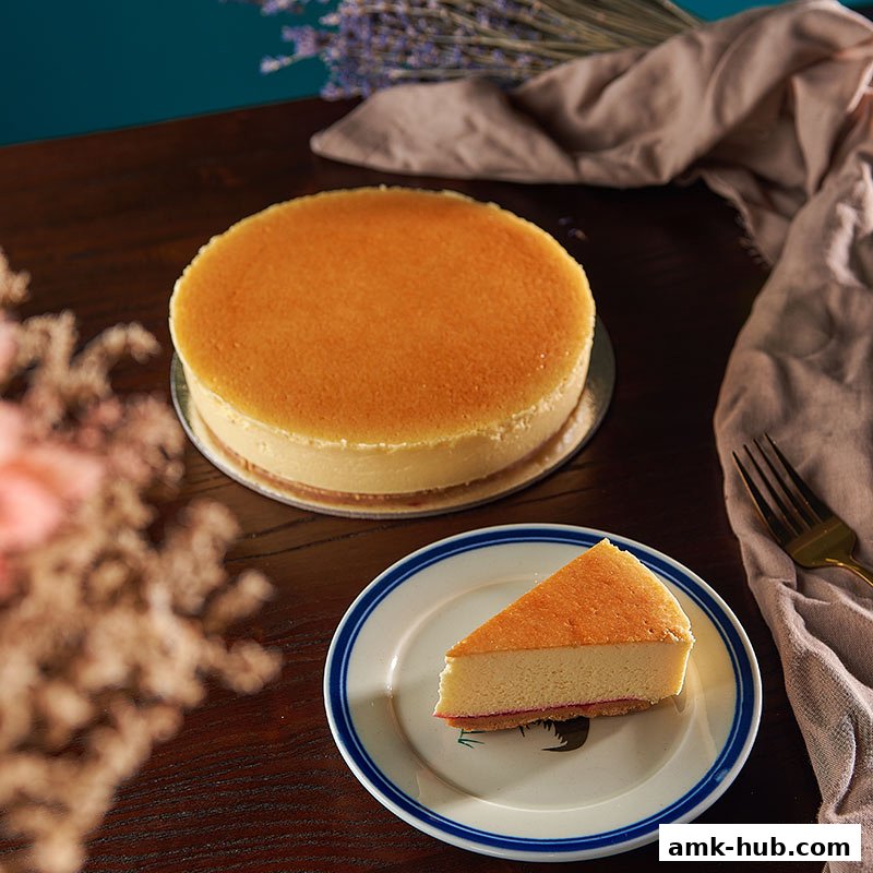 A whole cheesecake and a slice of cheesecake on a plate, with a fork and cloth.