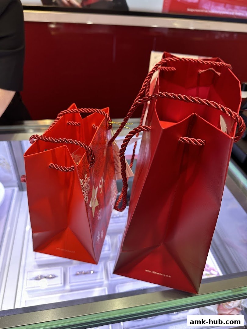 Two red shopping bags with rope handles sit on a display case in a jewelry store.