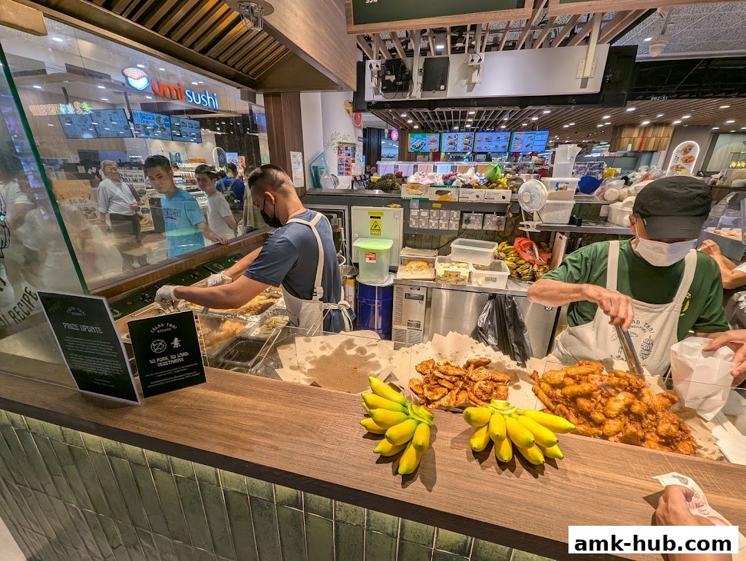 Staff serving fried bananas at a food stall with fresh bananas displayed.