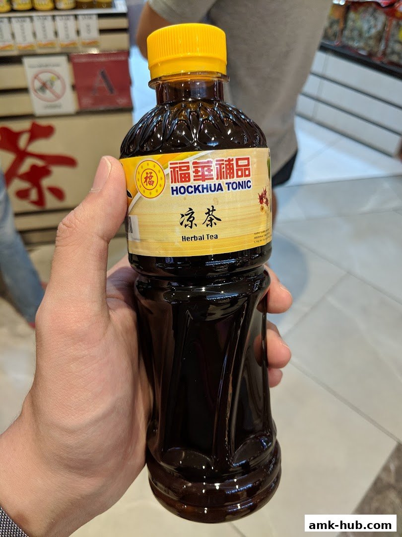 A hand holds a bottle of Hockhua Tonic Herbal Tea in a store.