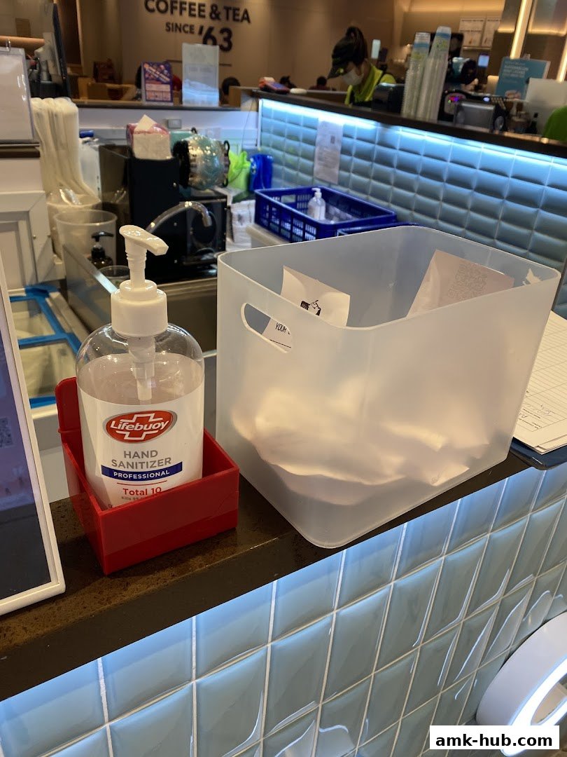 A hand sanitizer bottle and a bin are on a counter with a tiled backsplash.
